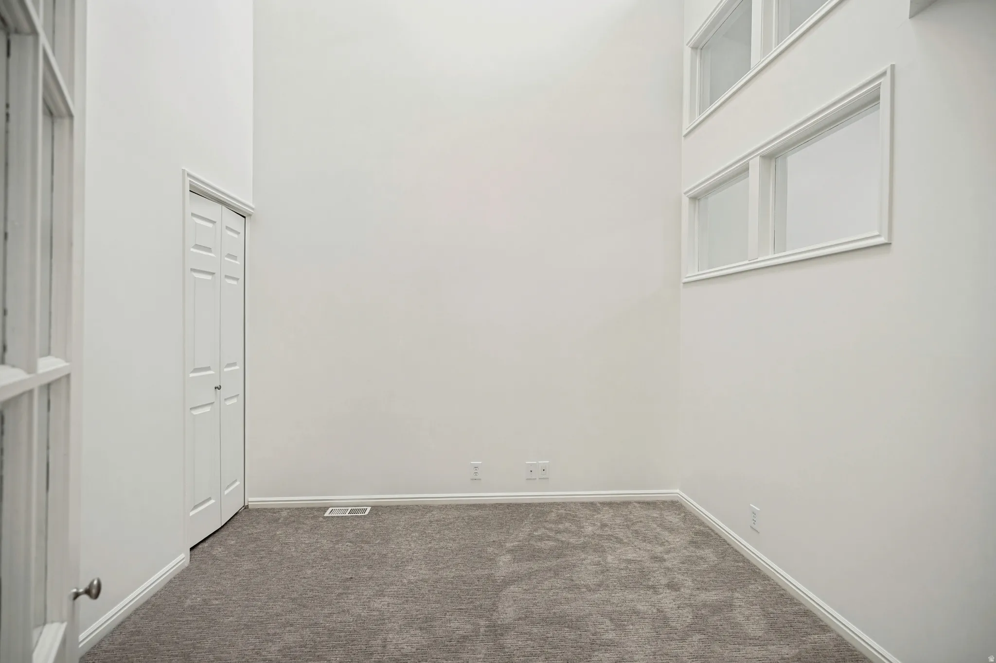 Room featuring high ceilings, light gray carpeting, and multiple windows