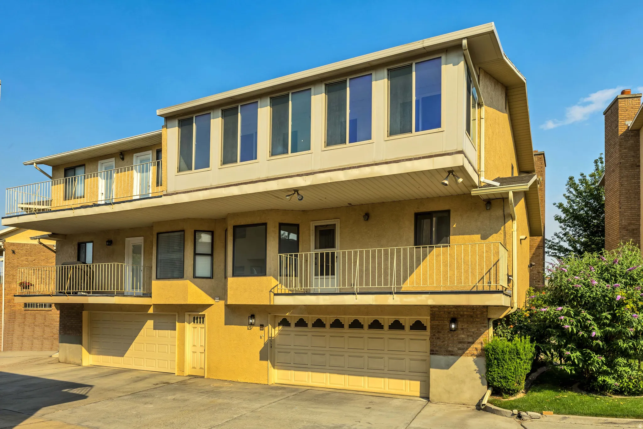 Multi-level facade with stucco exterior, multiple balconies with metal railings, varied window sizes, and integrated garage doors