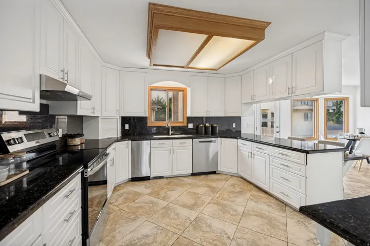Spacious kitchen featuring extensive white cabinetry, dark stone countertops, stainless steel appliances, a built-in dishwasher, and tiled flooring