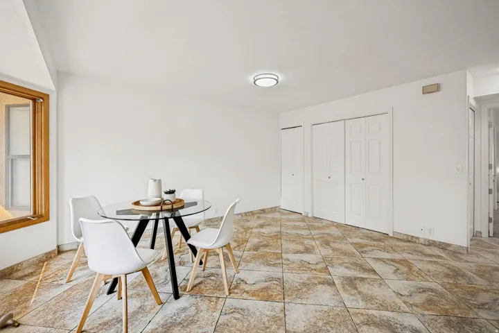 Spacious room featuring neutral wall tones, a large window with natural wood trim, and durable patterned tile flooring