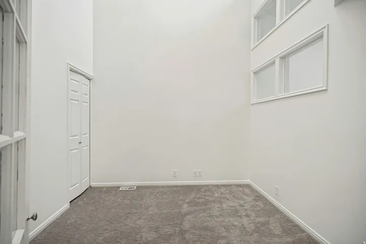 Room featuring high ceilings, light gray carpeting, and multiple windows
