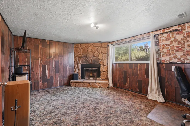 Corner stone fireplace with a raised hearth, wood-finish paneling, and a large window