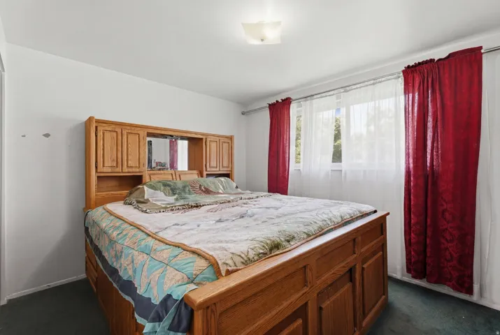 Light-filled bedroom featuring white walls, a large window with sheer and red drapes, and a ceiling-mounted light fixture