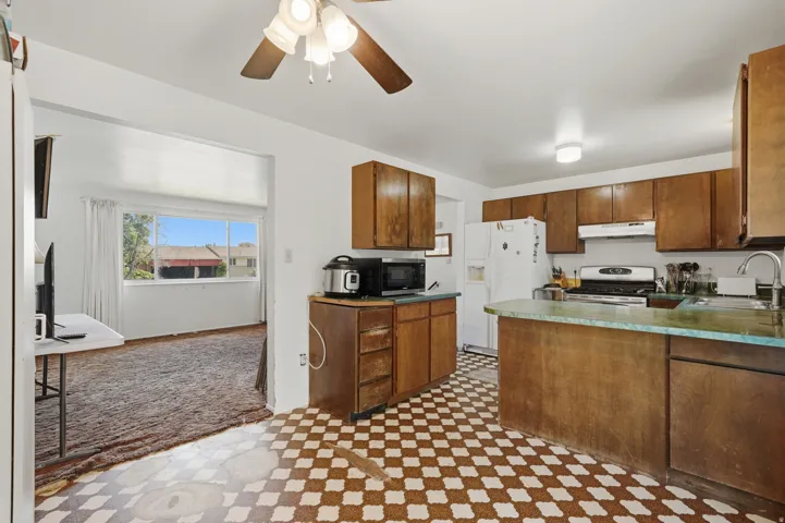 Kitchen featuring wood-finish cabinetry, checked flooring, and a ceiling fan with integrated lighting