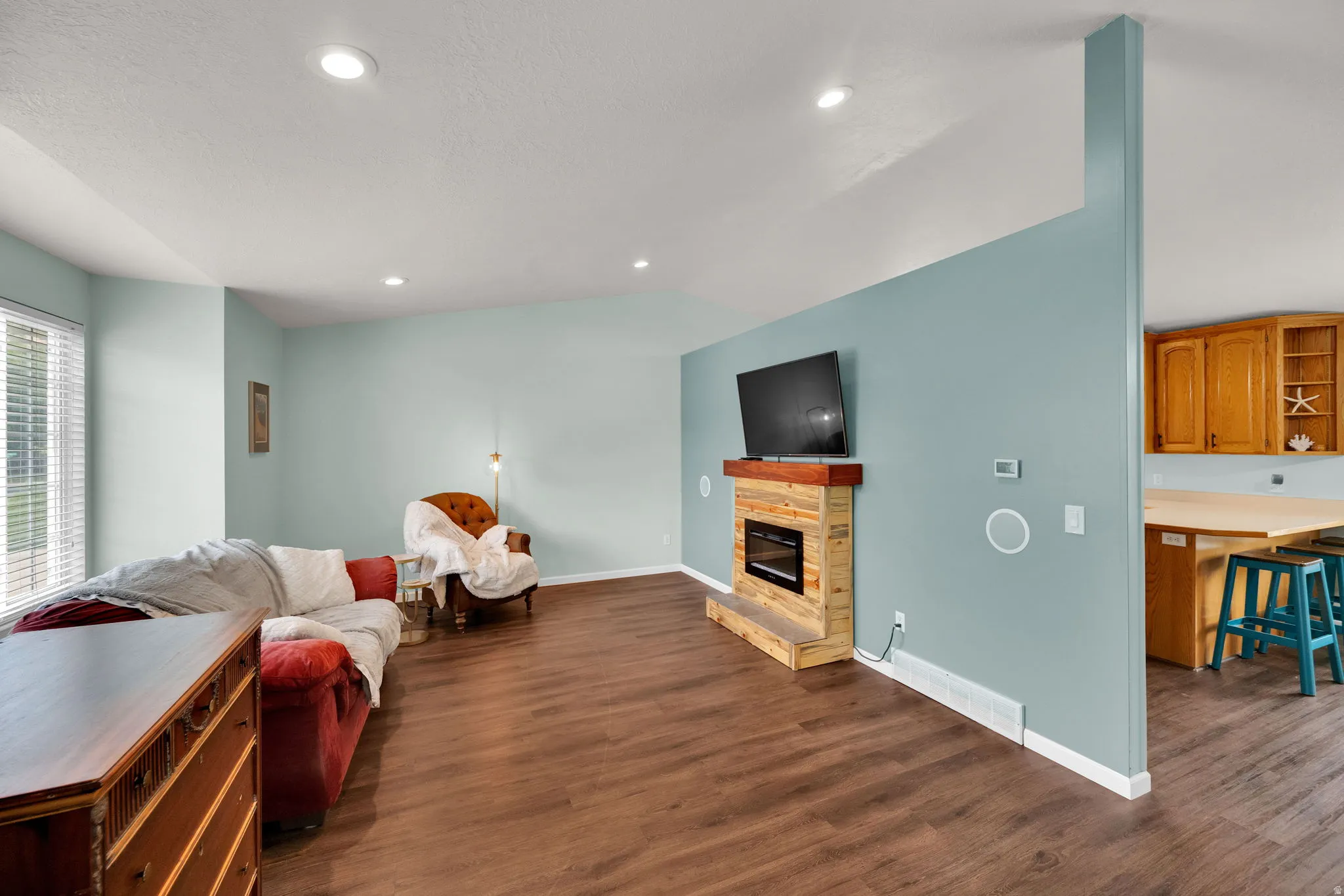 Spacious room featuring wood-finish flooring, recessed lighting, and a modern wall-mounted fireplace with a wood mantle