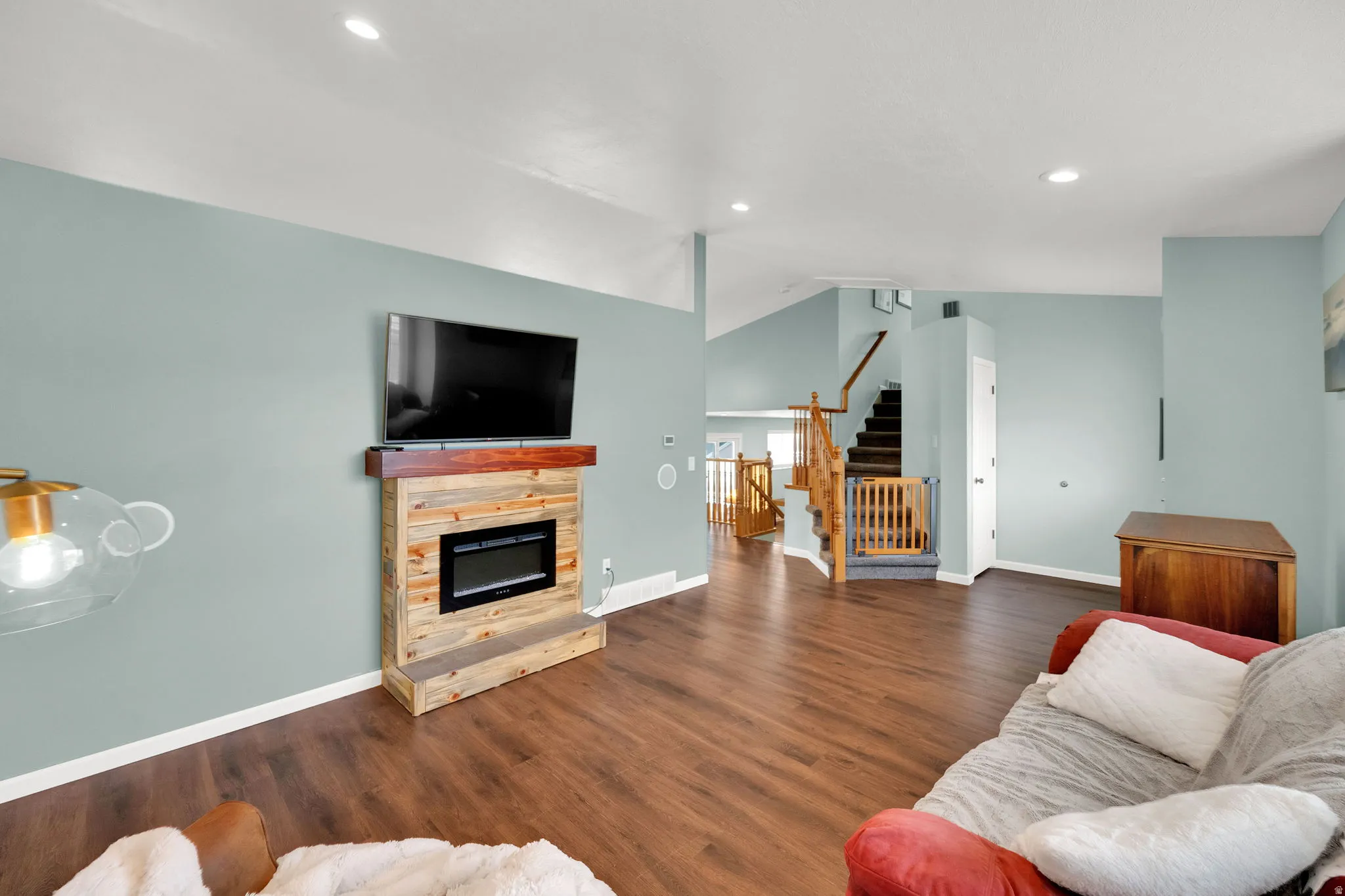 Living area featuring wood-finish flooring, a contemporary fireplace with a wood mantle, recessed lighting, and a staircase with wood railings