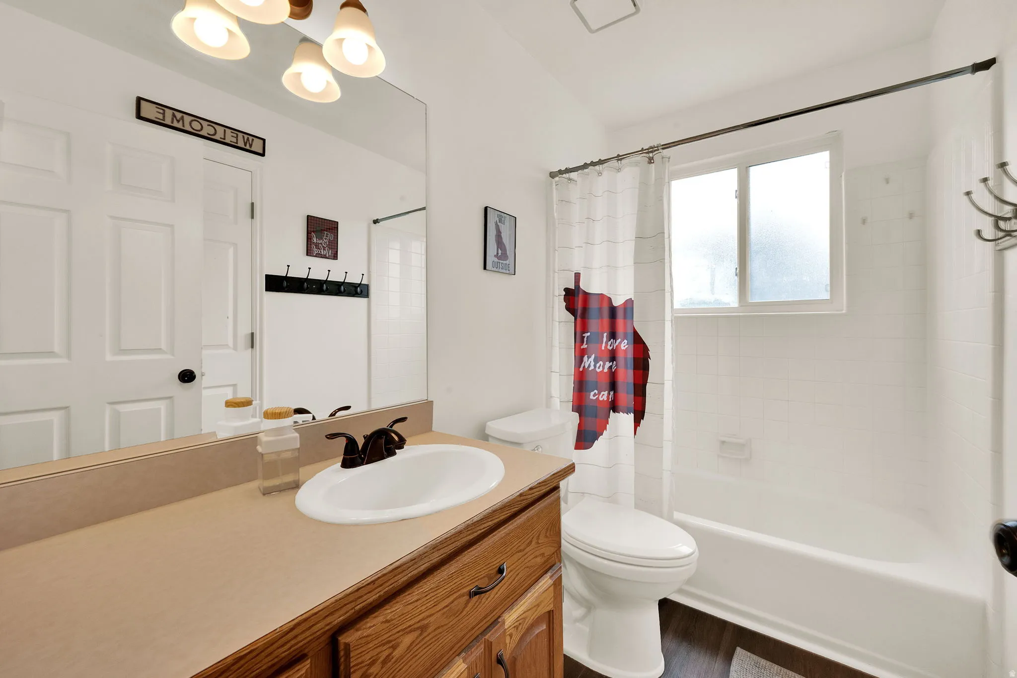 Bathroom featuring a wood-finish vanity with an integrated sink, a large wall mirror, and overhead vanity lighting