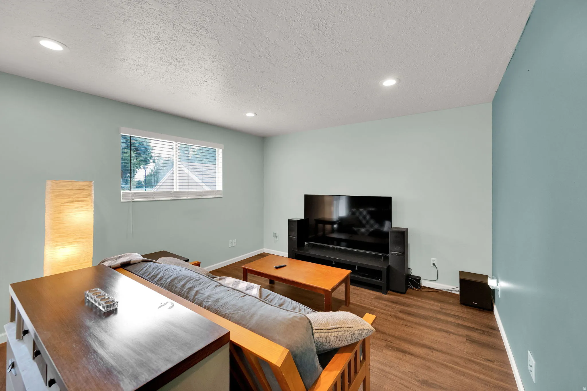 Spacious room featuring wood-finish flooring, light blue walls, a white ceiling with recessed lighting, and a window with white blinds