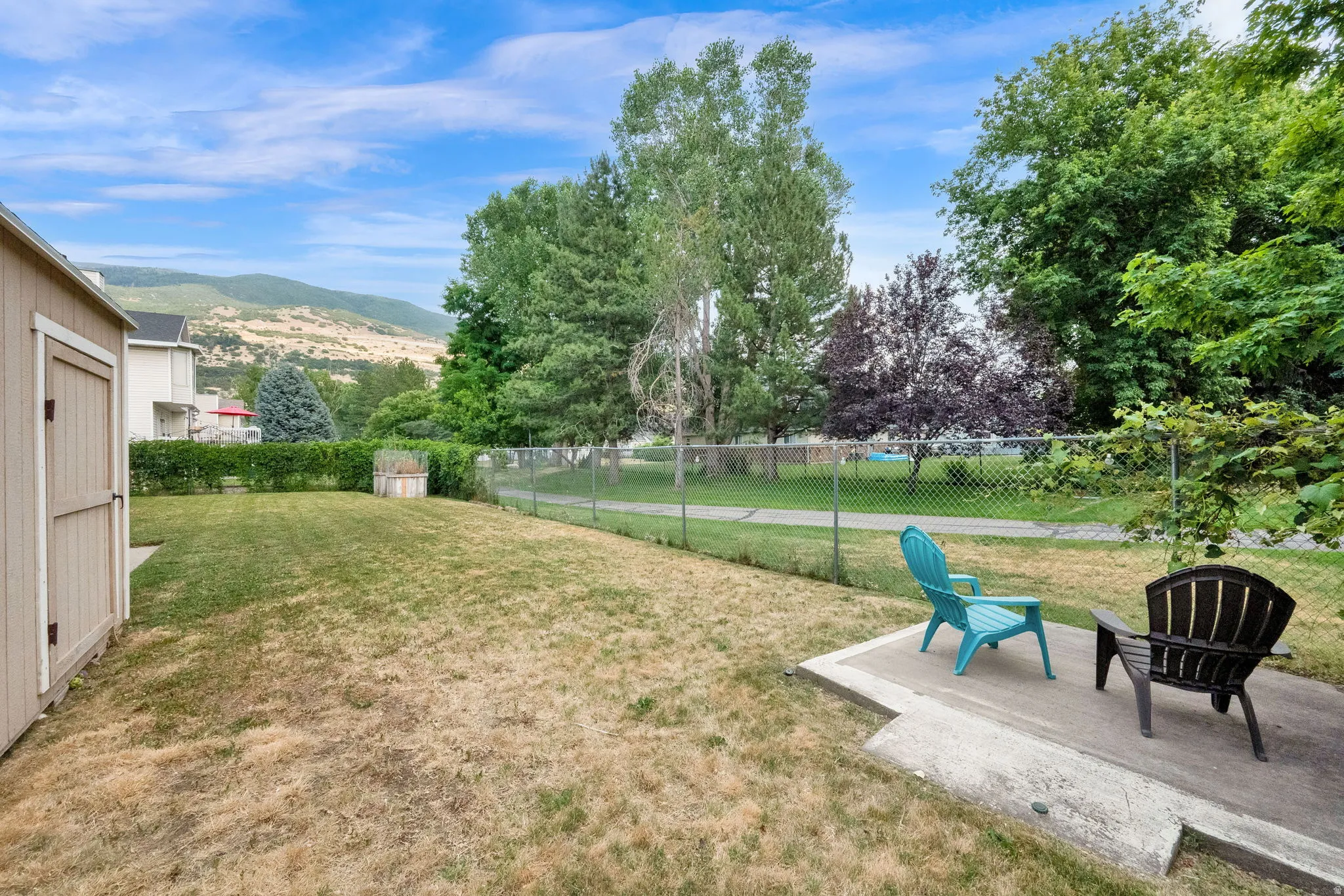 Expansive backyard with a concrete patio, wood-sided storage shed, and chain-link fencing