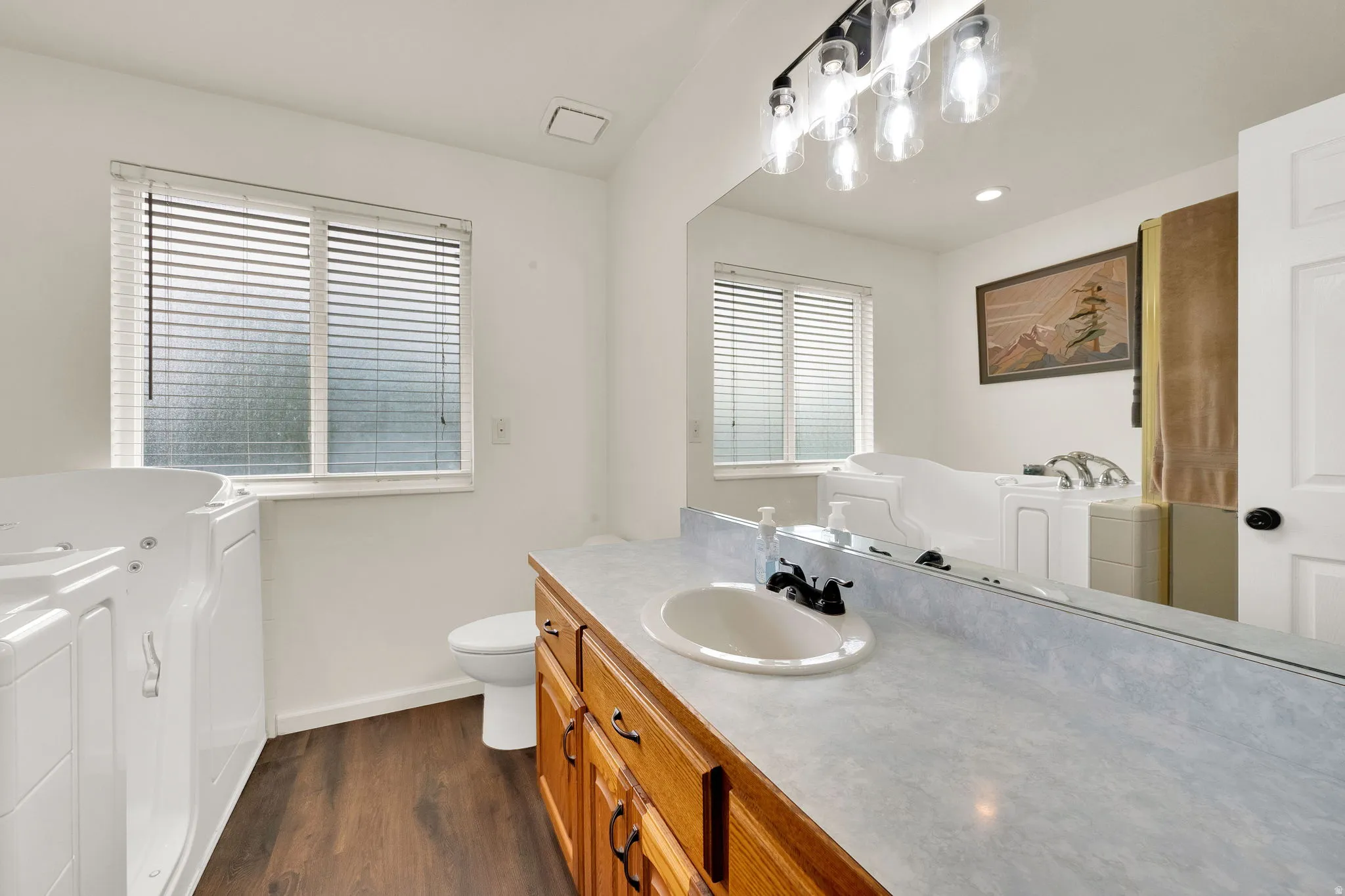 Bathroom with wood-finish flooring, a white vanity with wood cabinetry and a light-colored countertop, and a built-in white walk-in tub