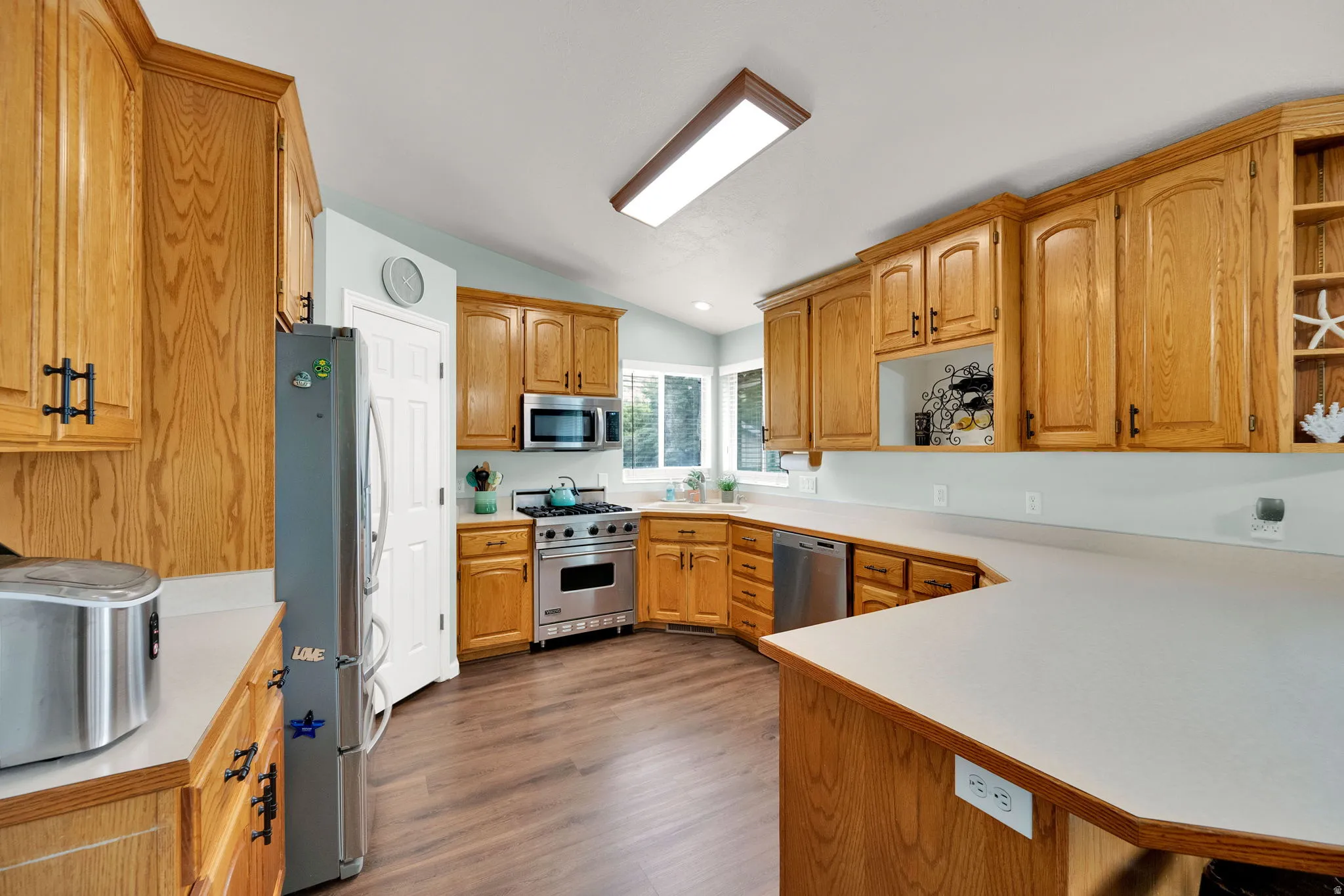 Kitchen featuring wood-finish flooring, abundant wood cabinetry, stainless steel appliances, and extensive countertop space