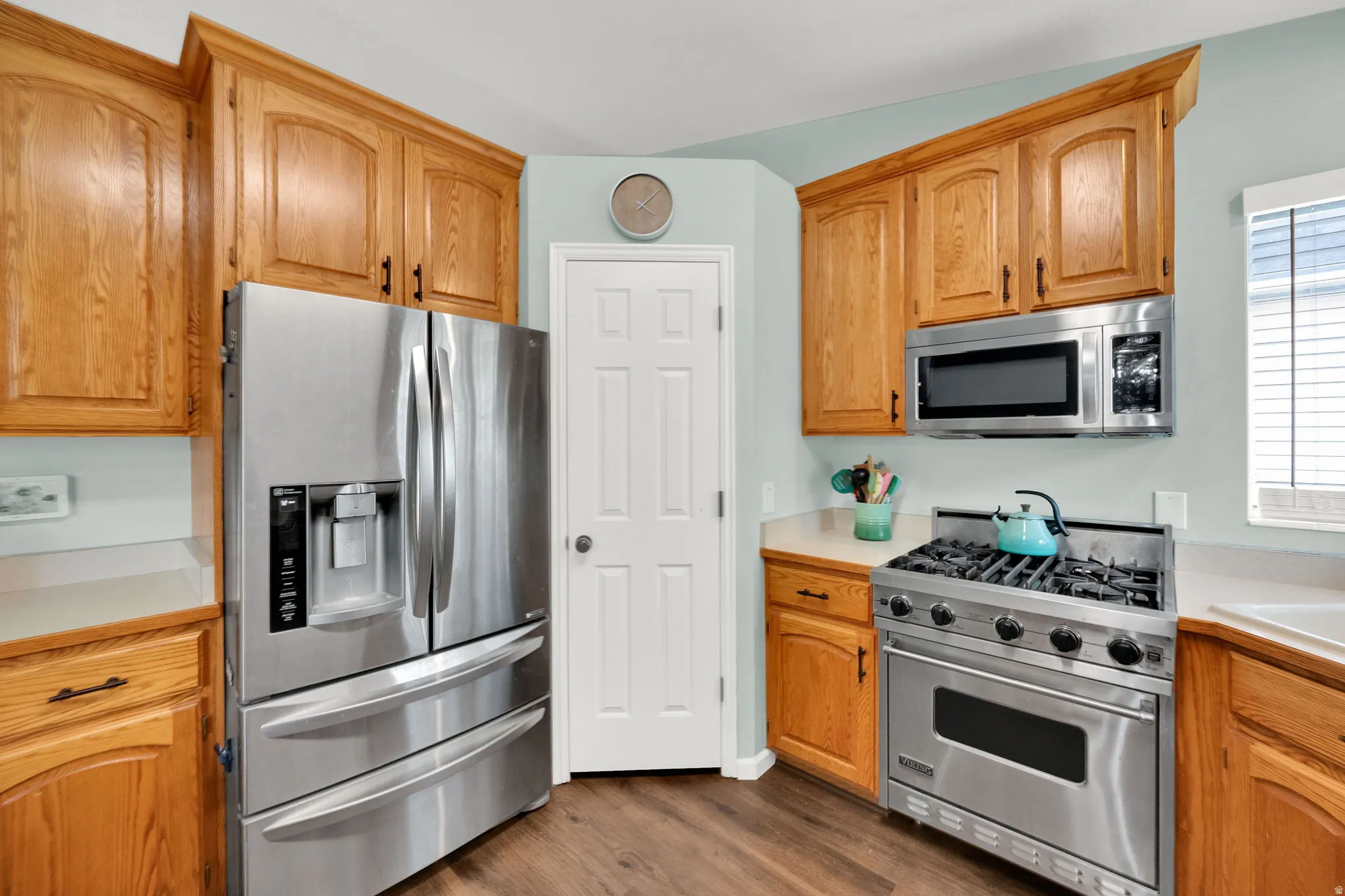Kitchen featuring extensive wood cabinetry, stainless steel French door refrigerator, stainless steel range with gas cooktop, stainless steel microwave, and light-toned countertops