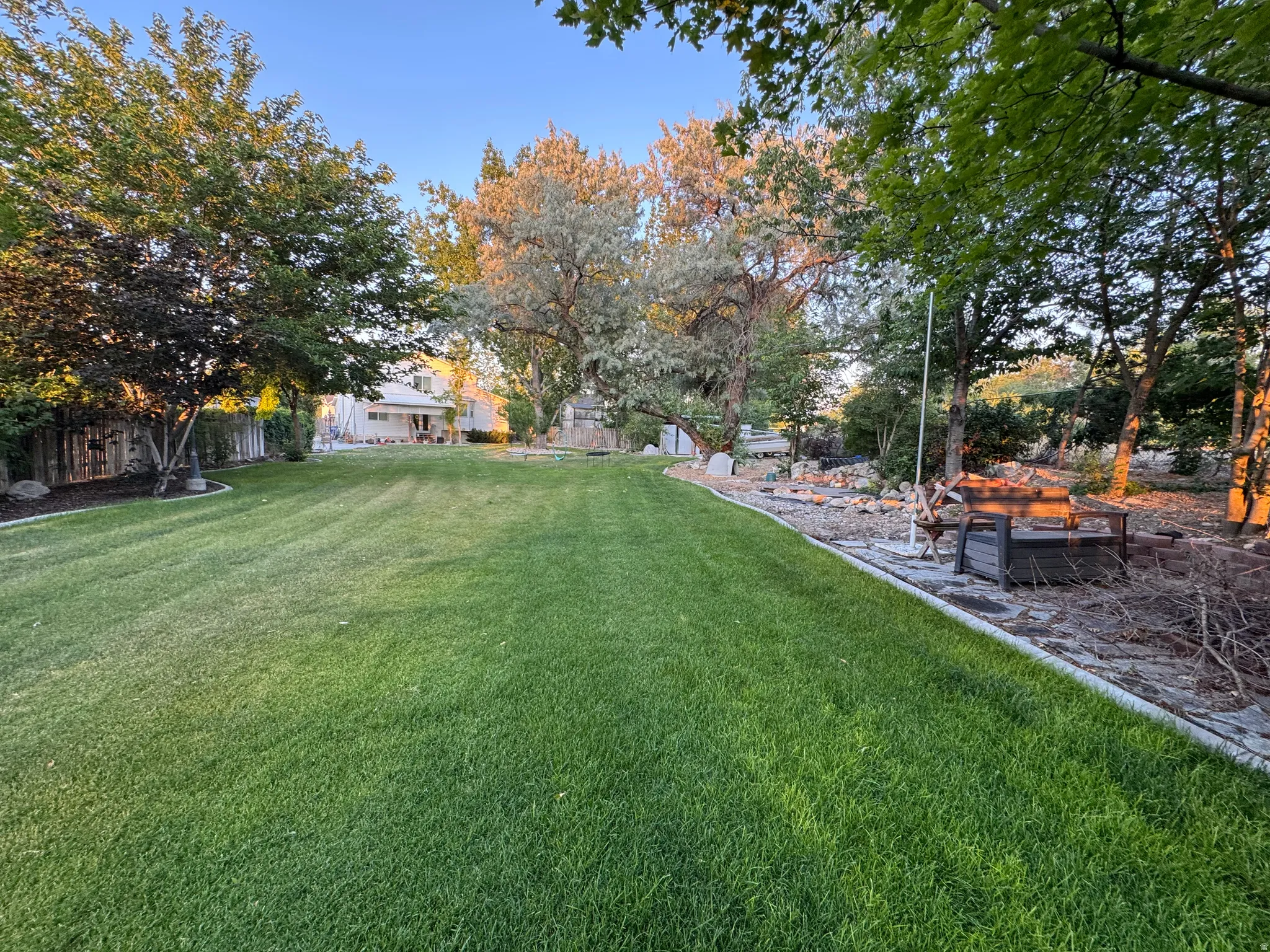 Expansive backyard featuring a manicured lawn, mature trees, and a concrete perimeter
