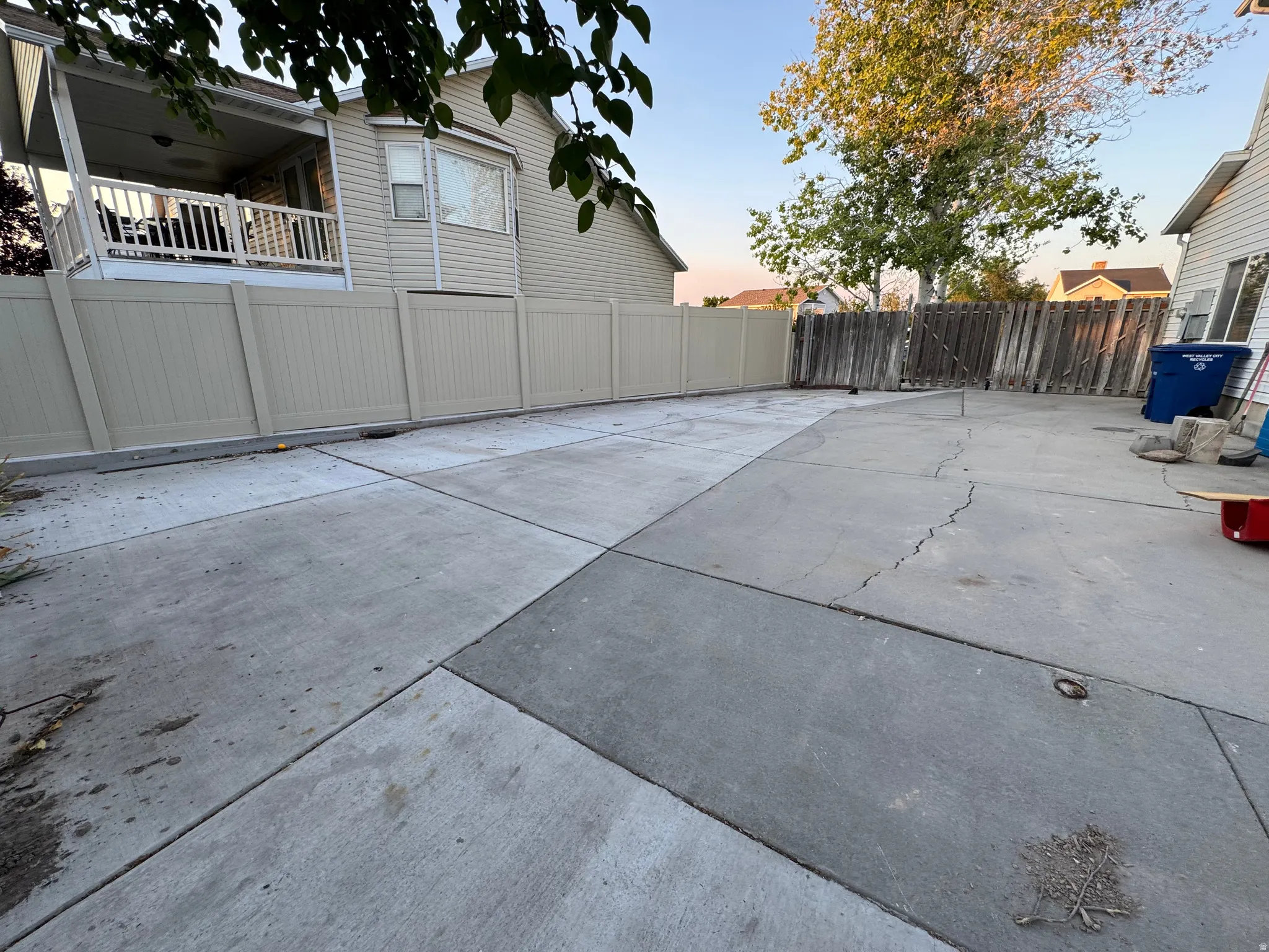 Expansive concrete patio area featuring a light-colored privacy fence and a rear porch with white railings