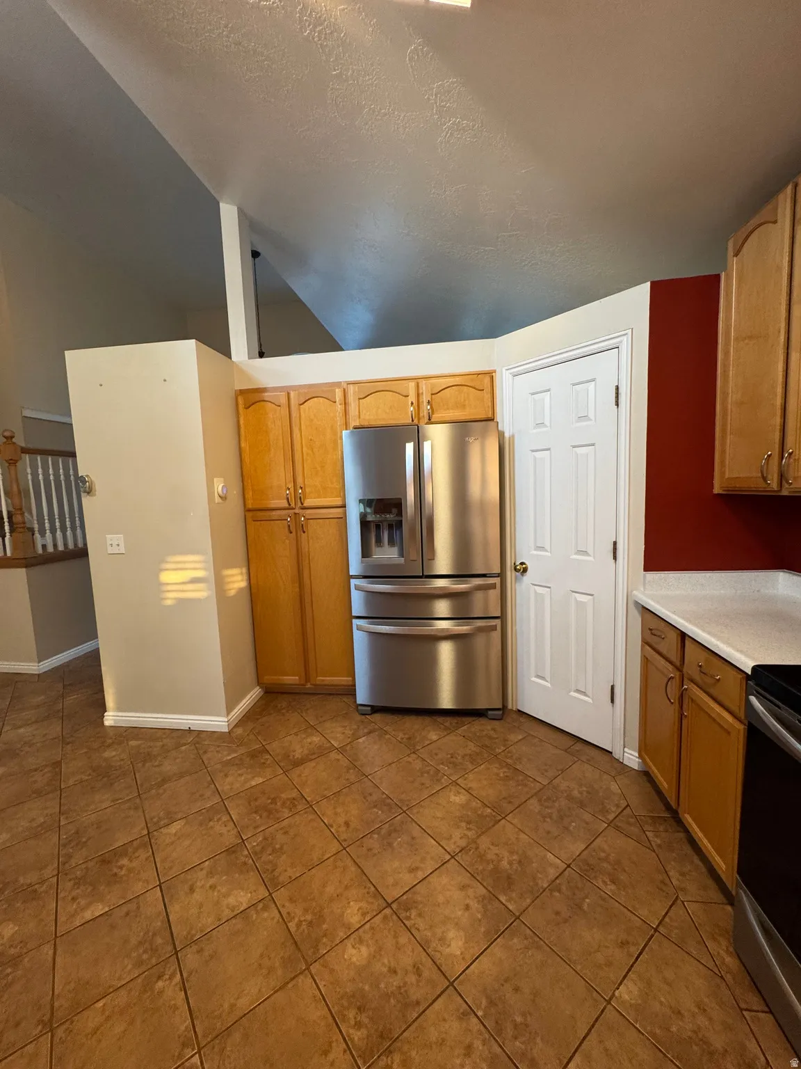 Kitchen area featuring stainless steel refrigerator, wood-finish cabinetry, light-toned countertops, and large format tile flooring
