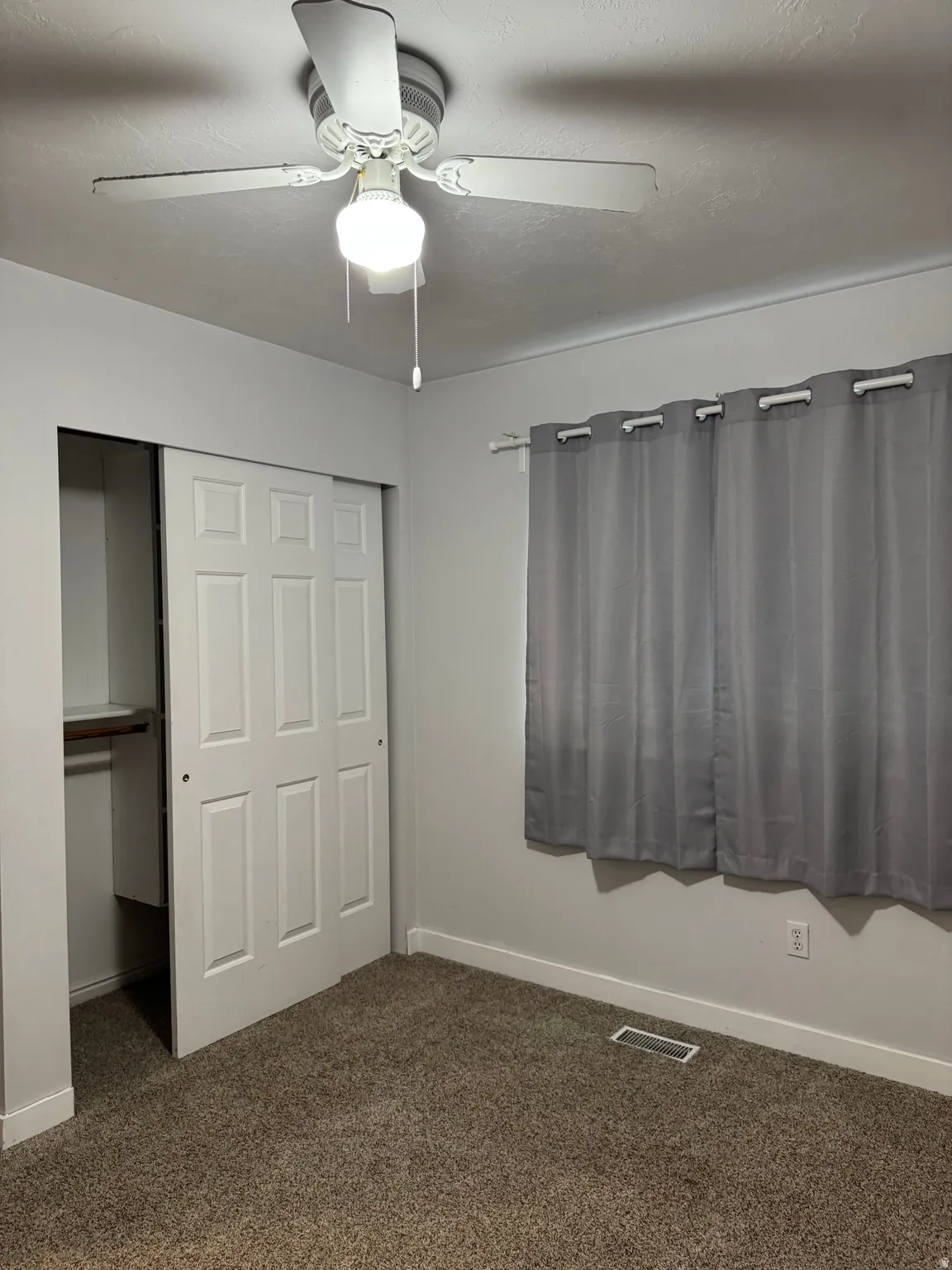 Interior room featuring neutral wall paint, textured carpeting, and a ceiling fan with integrated lighting