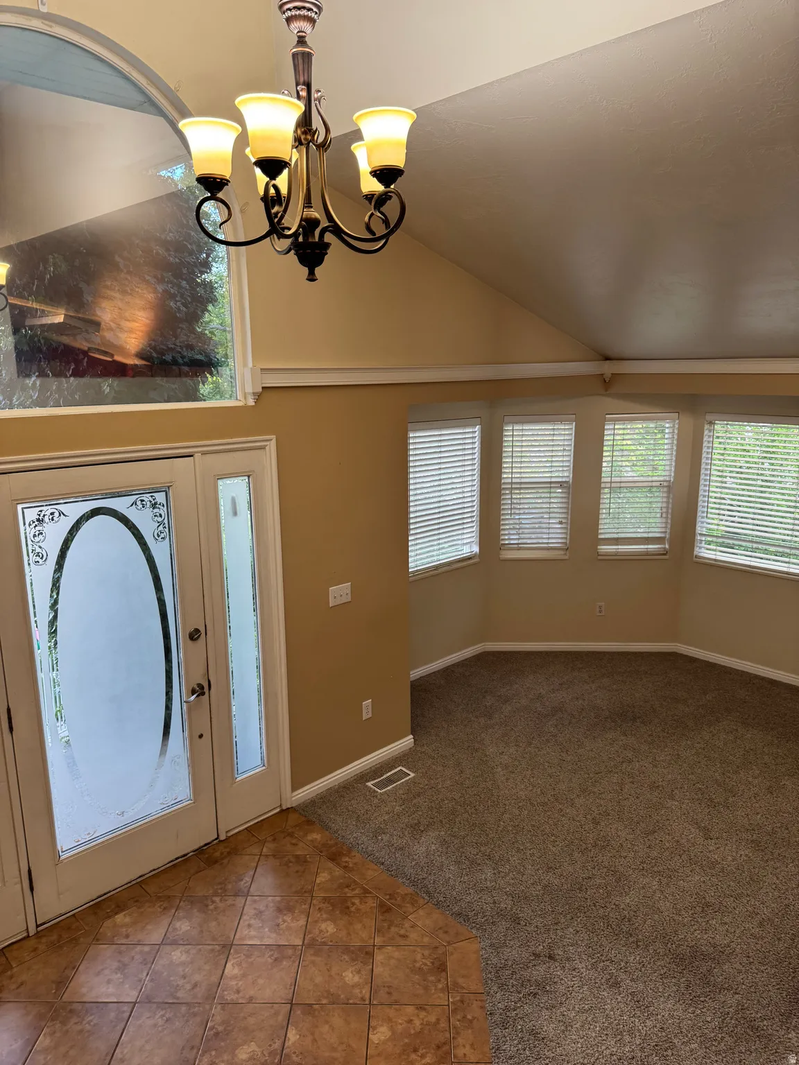 Entryway featuring tiled flooring, a decorative glass front door, and a vaulted ceiling with a chandelier
