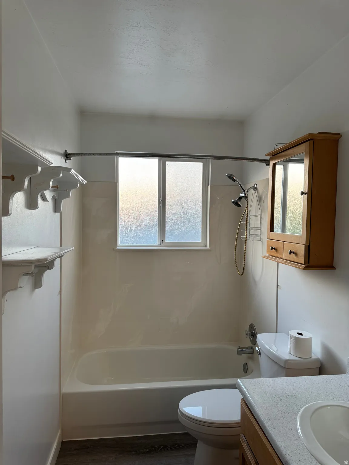 Bathroom featuring a white bathtub with a window, wood-finish flooring, a toilet, a vanity with an integrated sink, and a wall-mounted medicine cabinet