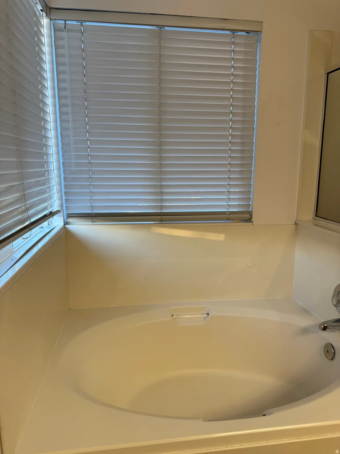 Built-in soaking tub with a window featuring horizontal blinds