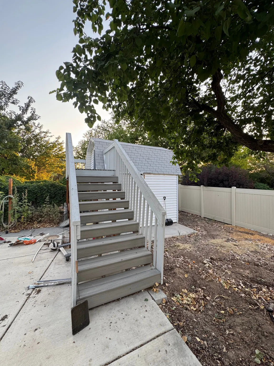 Outdoor stairs with white railings and gray treads, leading to a storage shed with white siding and a gray shingled roof