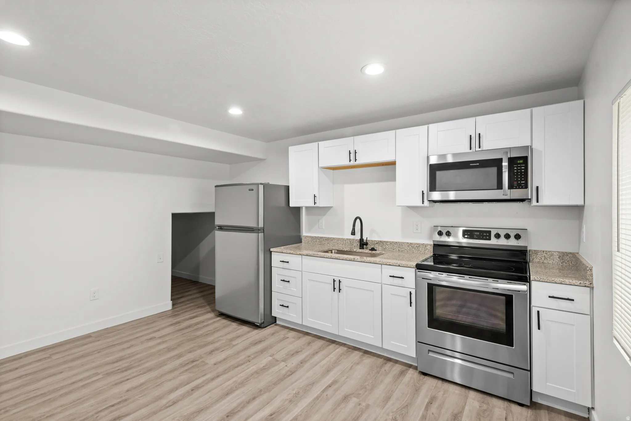 Kitchenette featuring white cabinetry, stainless steel appliances including a refrigerator, range, and microwave, and light-toned countertop