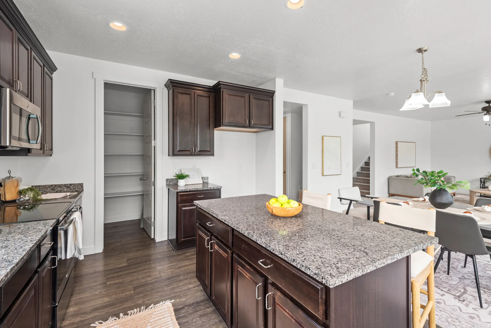 Modern kitchen featuring dark wood cabinetry, stainless steel appliances, granite countertops, a large center island with additional storage, and a walk-in pantry