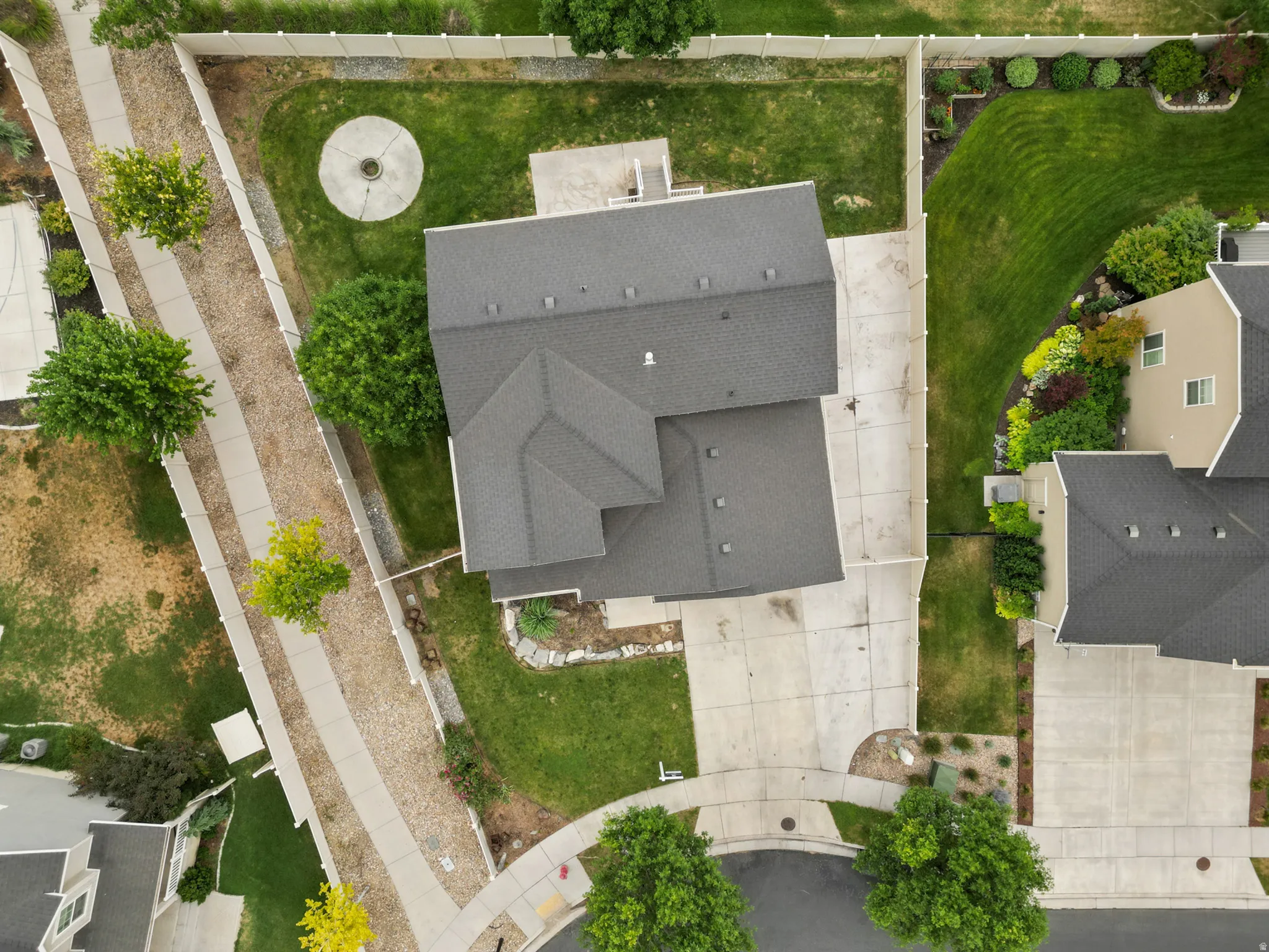Property featuring a dark shingle roof, concrete driveway, and established landscaping