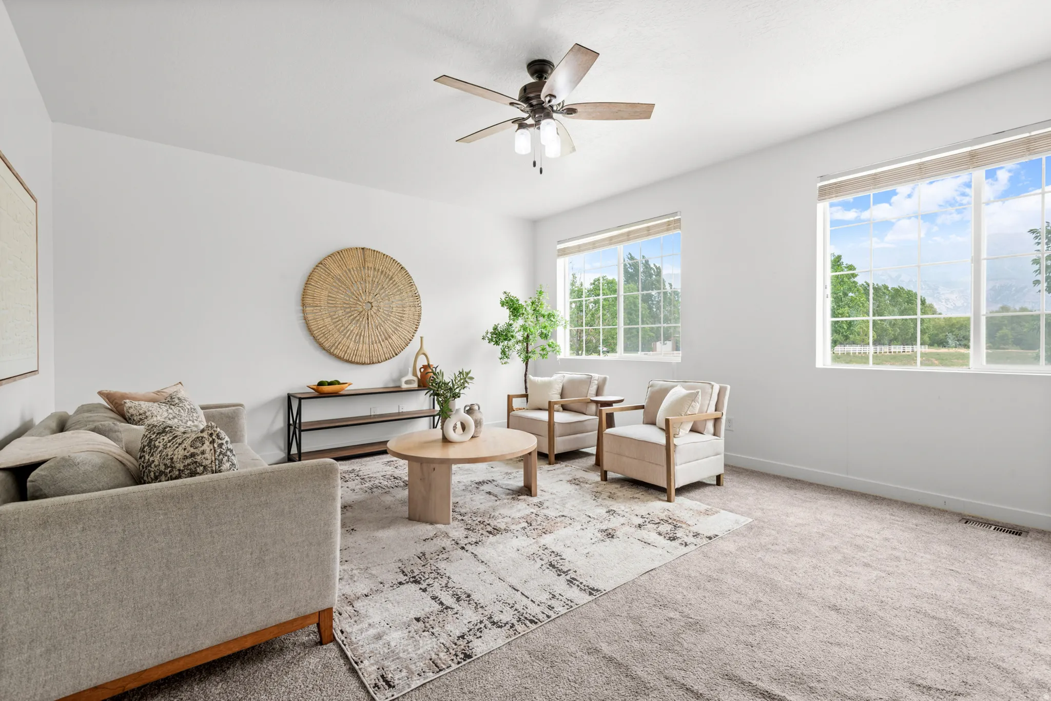 Bright interior space featuring multiple large windows, a ceiling fan with light fixture, light-toned carpeting, and white wall finishes