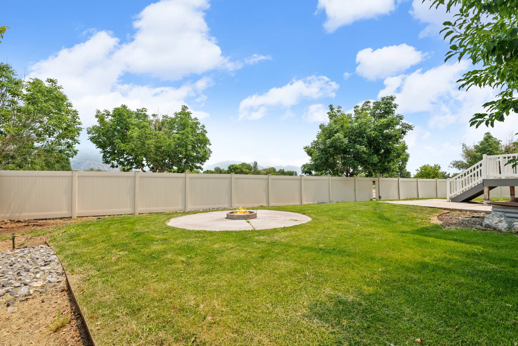 Expansive backyard featuring a lush lawn, a circular concrete patio with a built-in fire pit, and a tan privacy fence