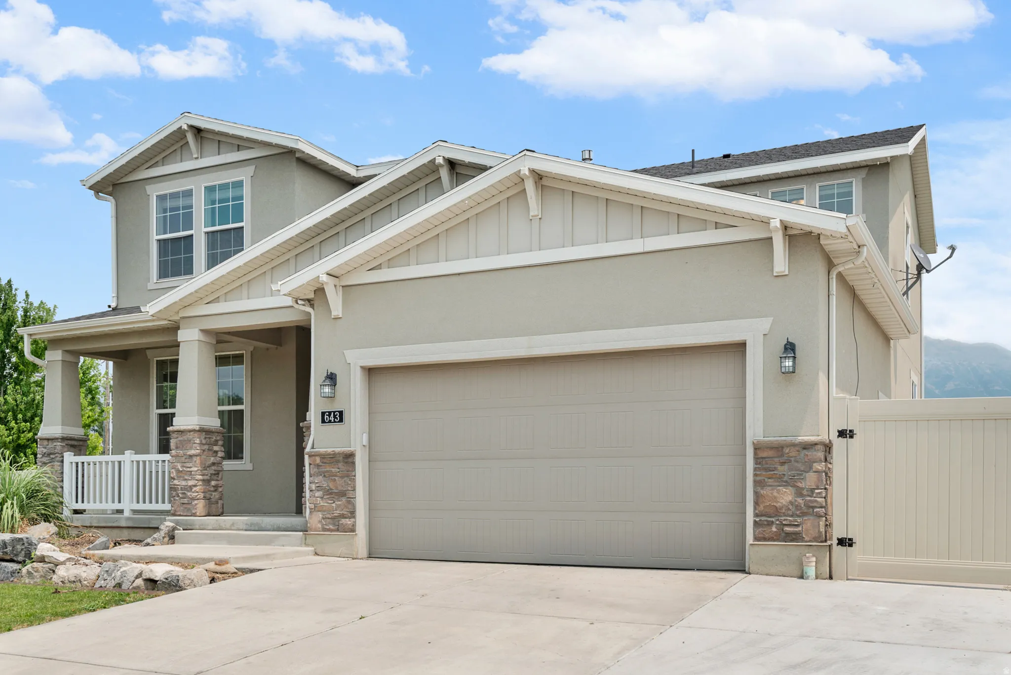 Contemporary two-story residence featuring a two-car garage, stone veneer accents, and a covered porch with white railing