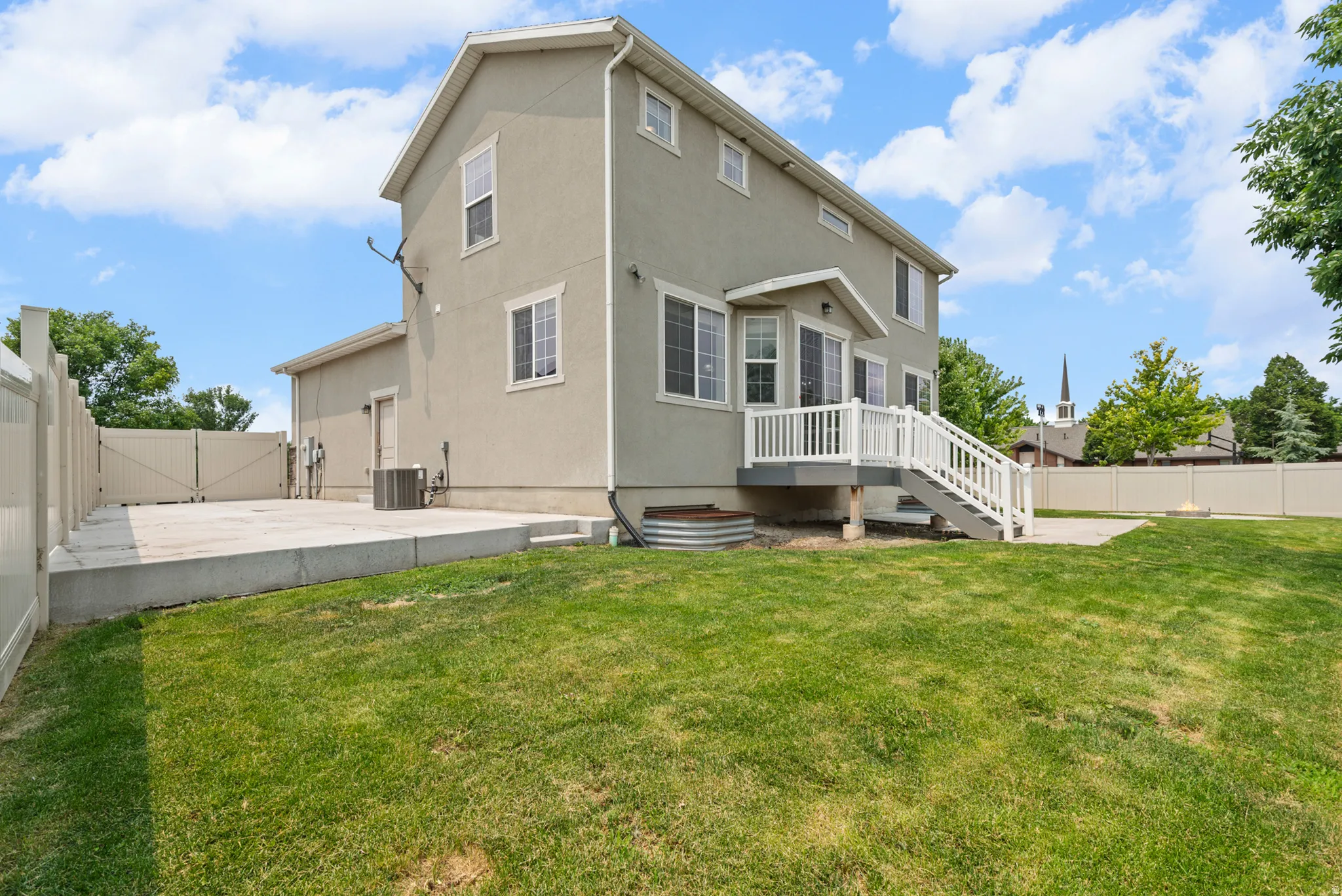 Spacious rear yard with a green lawn, concrete patio, and privacy fencing