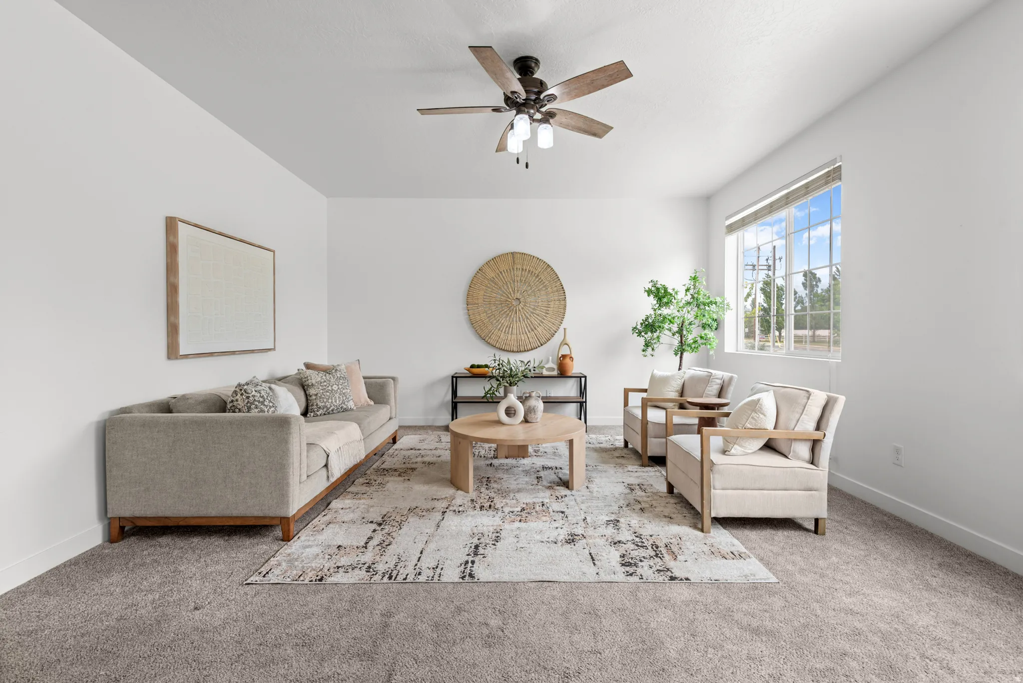 Spacious living area featuring neutral carpeting, a ceiling fan with integrated lighting, and multiple large windows providing ambient illumination