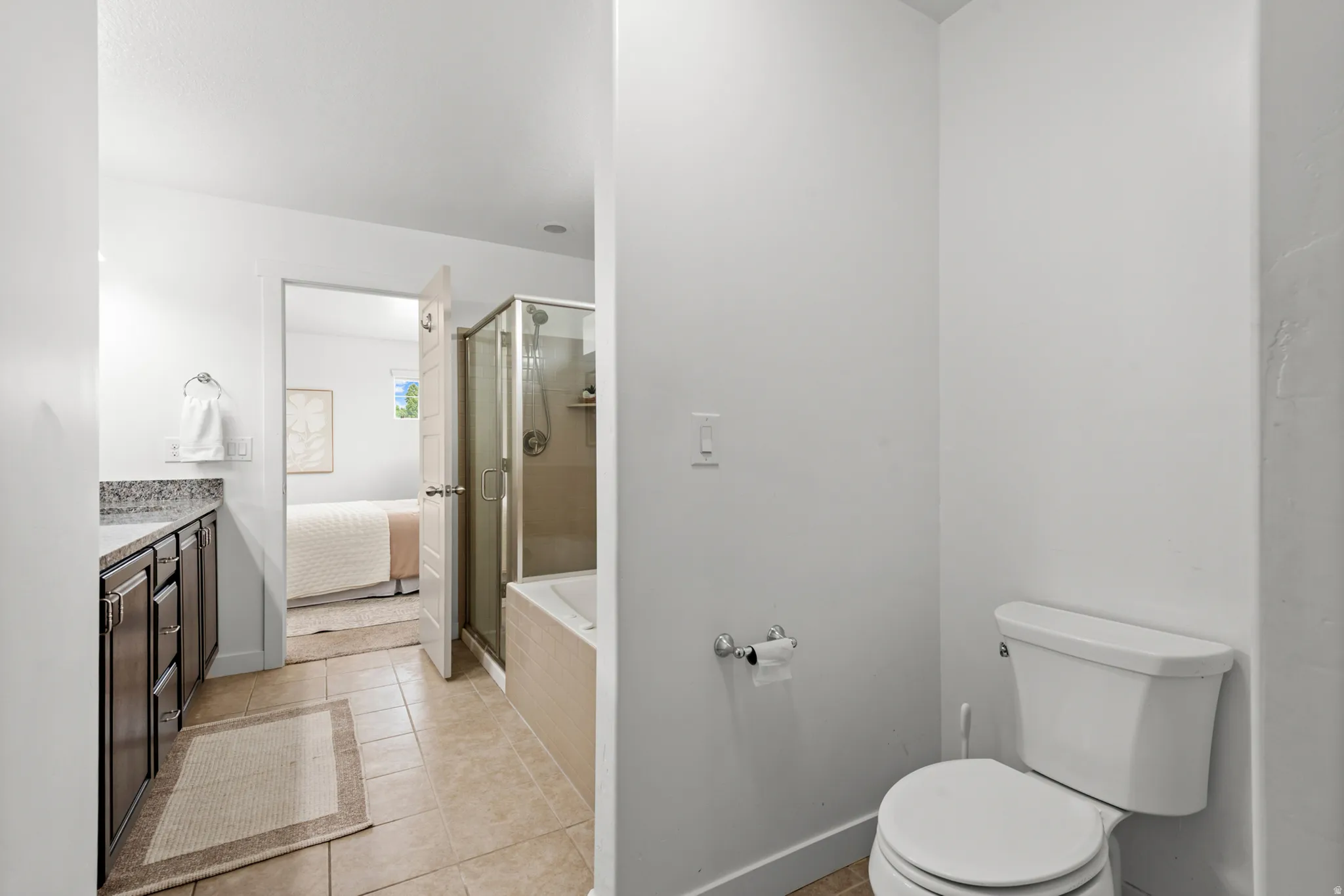 Bathroom featuring a built-in tub with a glass-enclosed shower, a vanity with dark cabinetry and a stone-finish countertop, and tile flooring