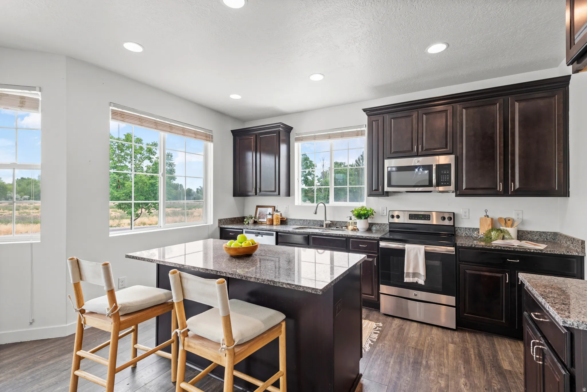 Kitchen featuring dark wood cabinetry, stainless steel appliances, granite countertops, a central island with bar seating, and wood-finish flooring