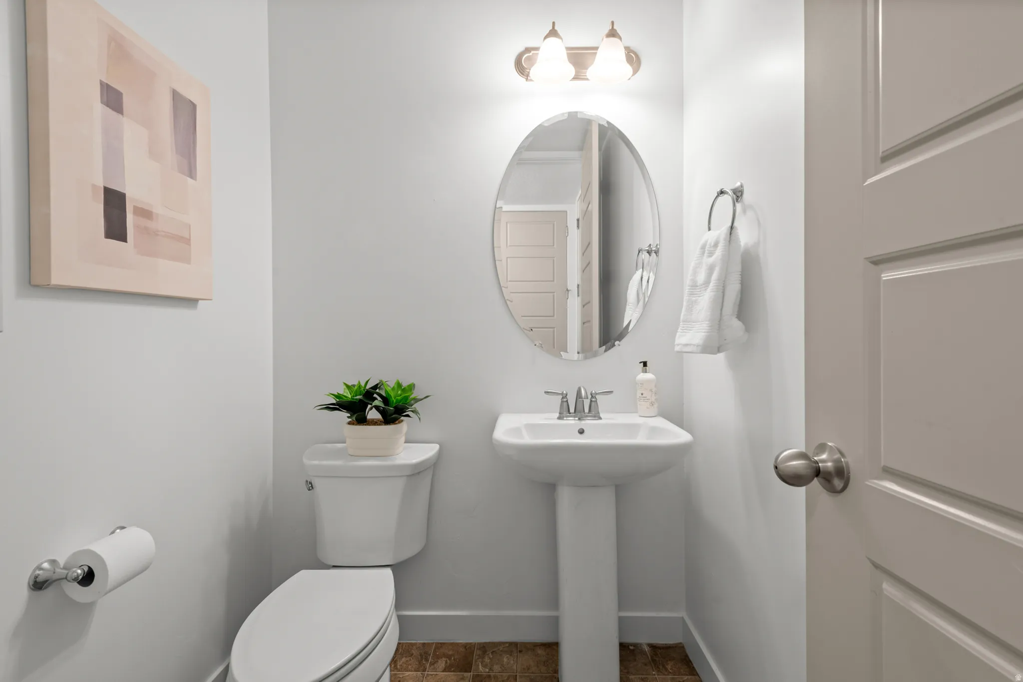 Contemporary powder room featuring a pedestal sink, oval mirror, and a two-bulb vanity light fixture
