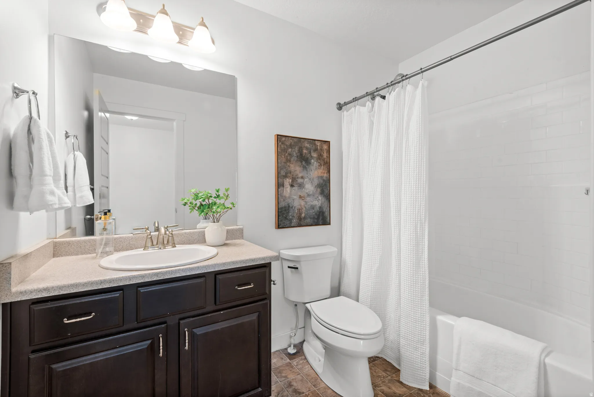 Bathroom featuring a dark wood-finish vanity with an integrated sink, a large mirror, and a three-light fixture