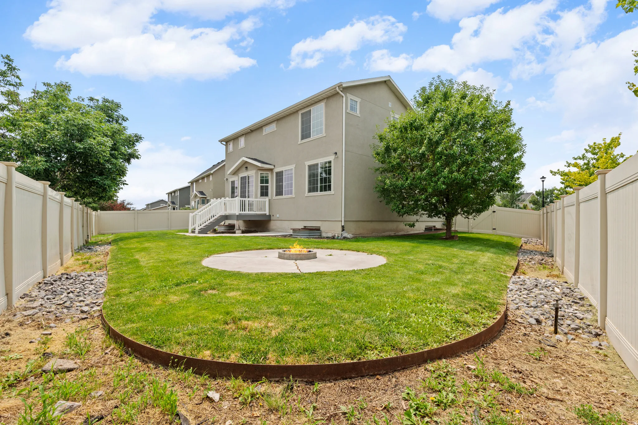 Rear exterior featuring a manicured lawn, full privacy fencing, and a concrete patio with a built-in fire pit