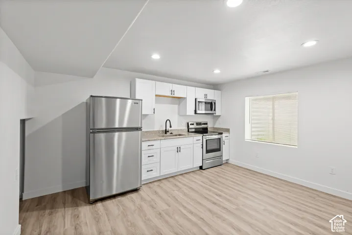 Contemporary kitchen area featuring white cabinetry, stainless steel appliances, granite-style countertops, wood-finish flooring, and recessed lighting