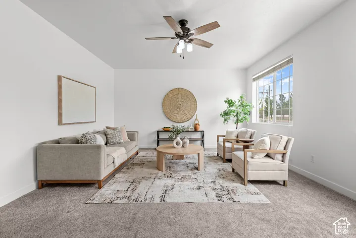 Spacious living area featuring neutral carpeting, a ceiling fan with integrated lighting, and multiple large windows providing ambient illumination