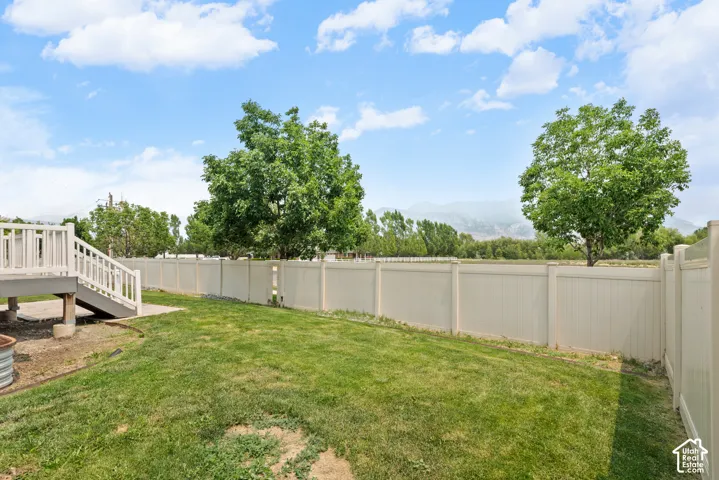 Expansive backyard featuring a large green lawn, a multi-level deck with white railings, a tan privacy fence, and mature trees