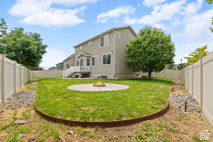 Rear exterior featuring a manicured lawn, full privacy fencing, and a concrete patio with a built-in fire pit