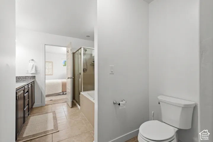 Bathroom featuring a built-in tub with a glass-enclosed shower, a vanity with dark cabinetry and a stone-finish countertop, and tile flooring