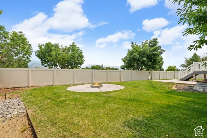 Expansive backyard featuring a lush lawn, a circular concrete patio with a built-in fire pit, and a tan privacy fence
