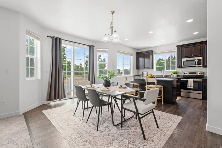 Open-concept dining area featuring wood-finish flooring, a contemporary chandelier, and ample natural light from multiple windows and a sliding glass door