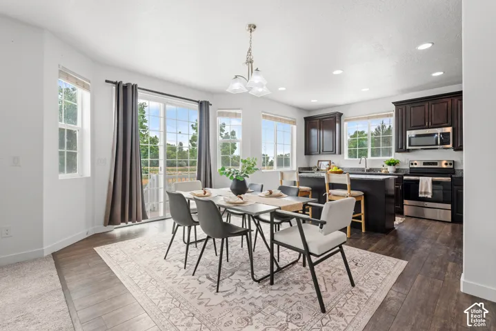 Open-concept dining area featuring wood-finish flooring, a contemporary chandelier, and ample natural light from multiple windows and a sliding glass door