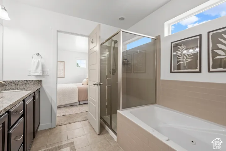 Bathroom featuring a built-in tub, separate glass-enclosed shower, single vanity with a stone countertop, and tile flooring