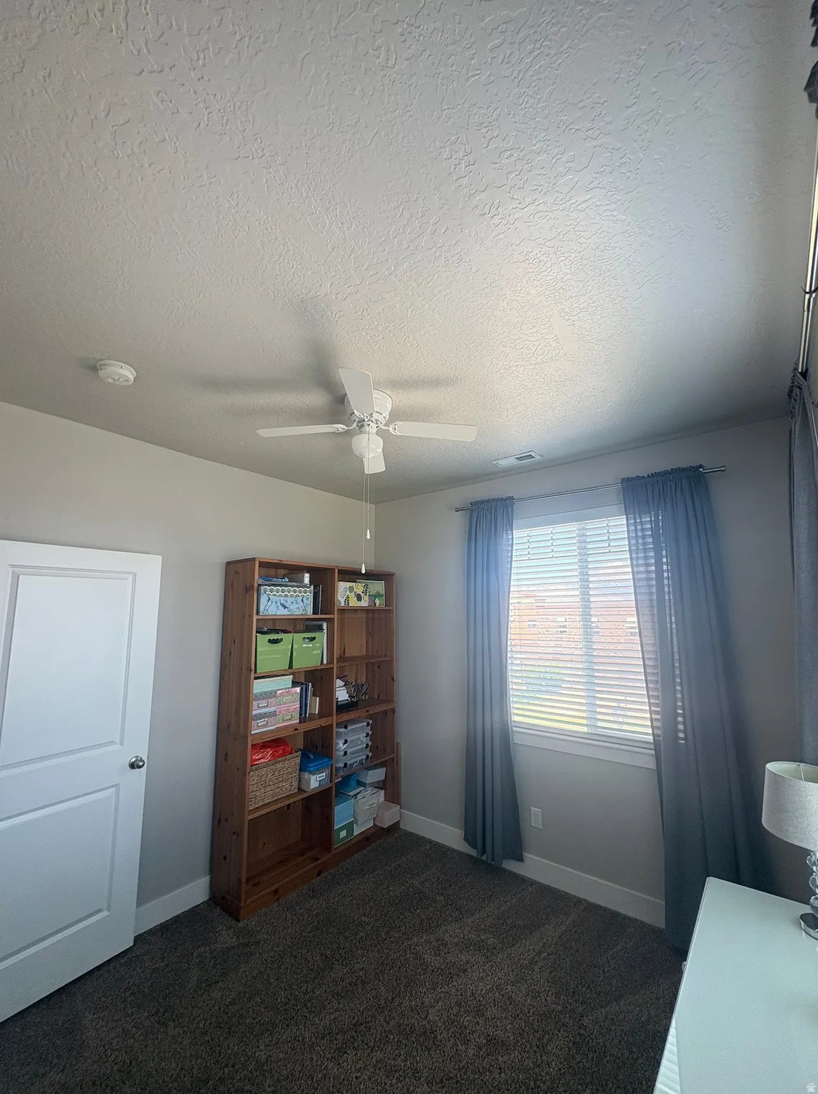 Carpeted room featuring a ceiling fan, a window with blinds and drapes, and a white interior door