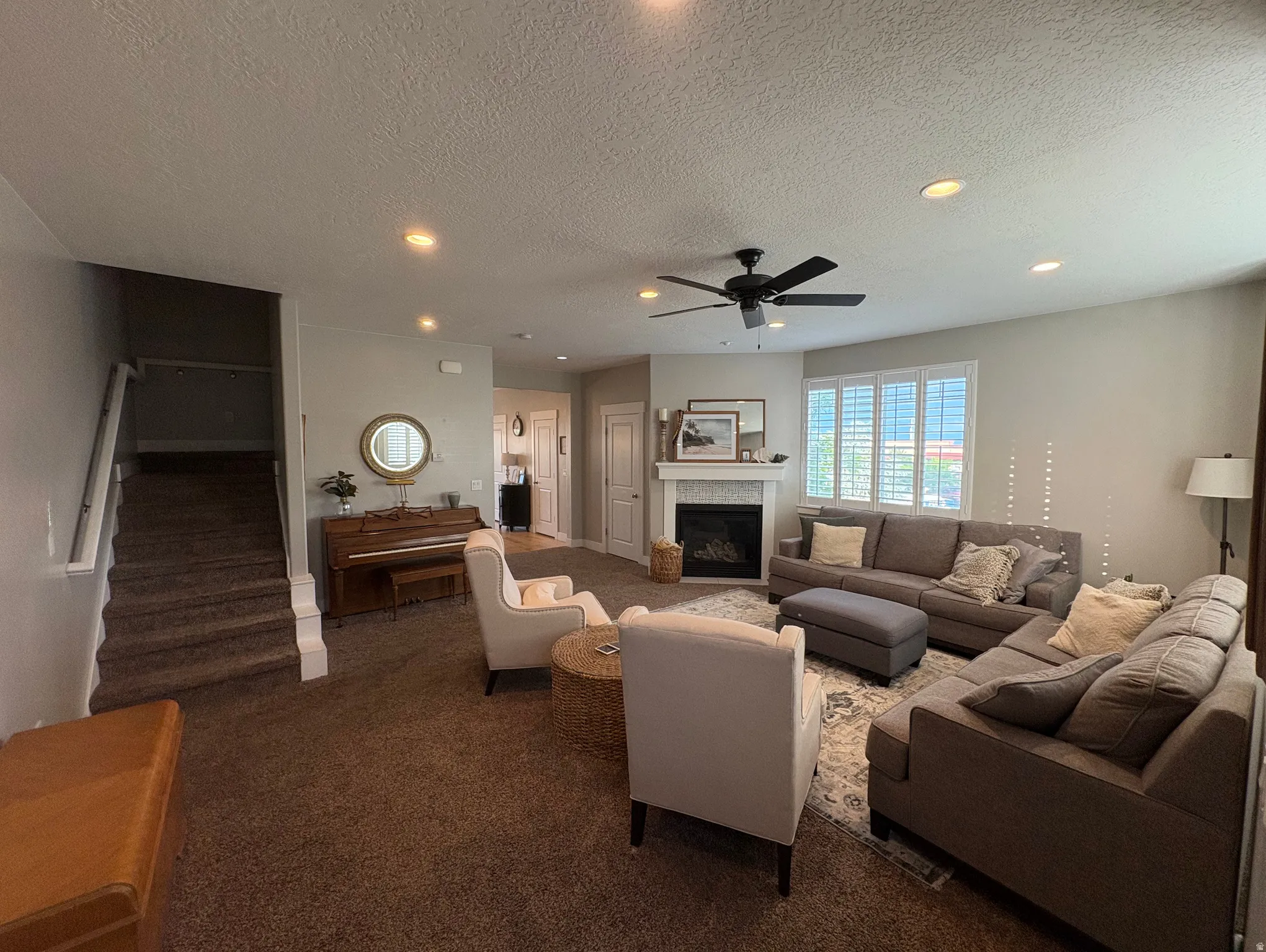 Spacious living area featuring neutral carpeting, recessed lighting, a ceiling fan, and a fireplace with a stone surround and white mantel