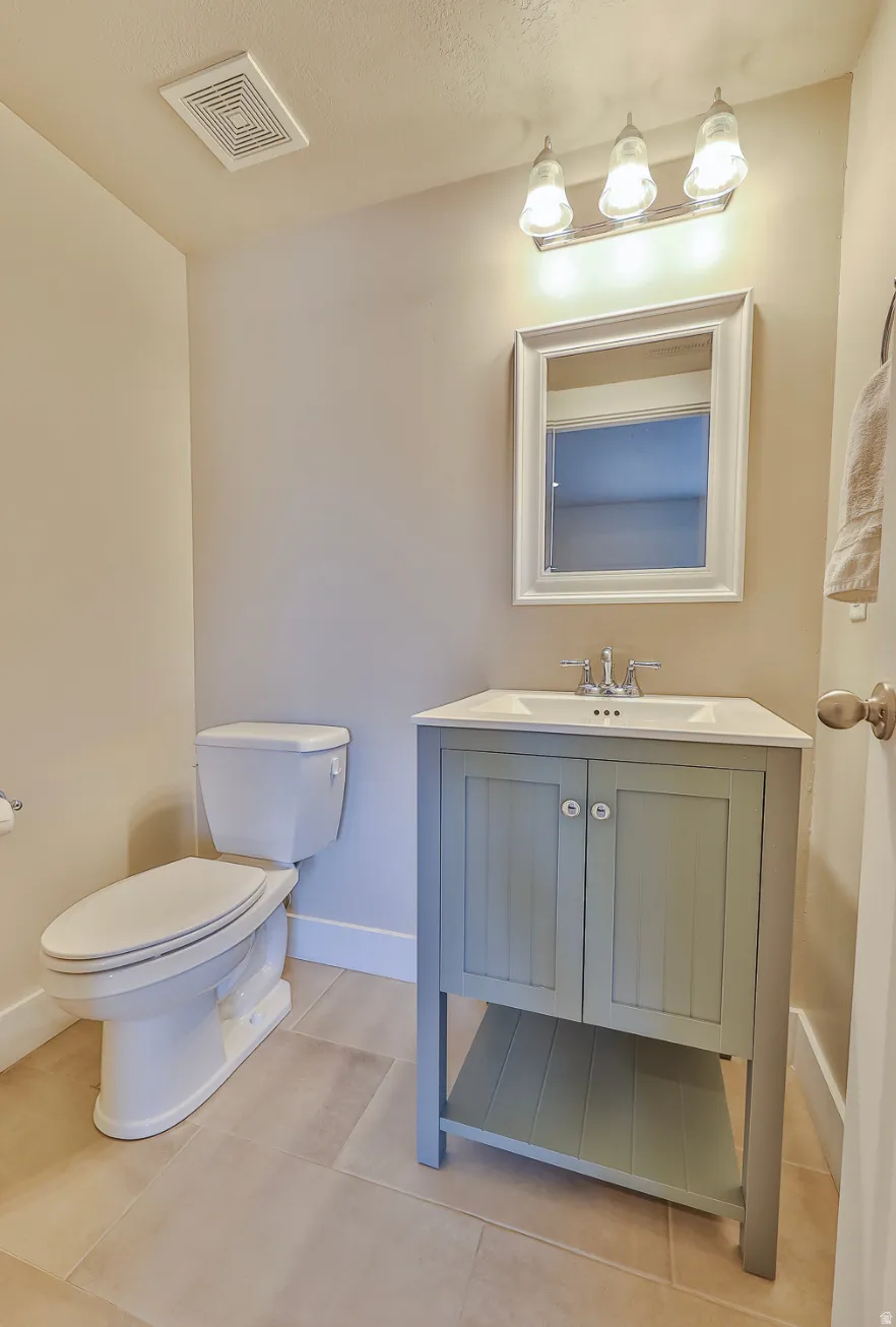 Bathroom featuring a sage green vanity with white ceramic top, rectangular framed mirror, three-light vanity fixture, and large format floor tiles