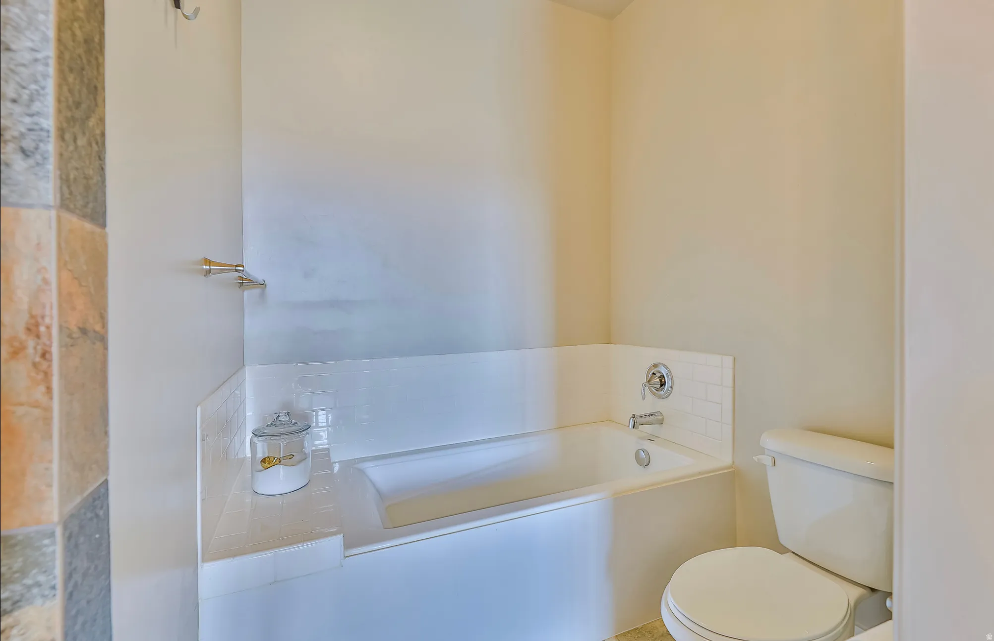 Bathtub with subway tile surround, polished chrome fixtures, and adjacent commode